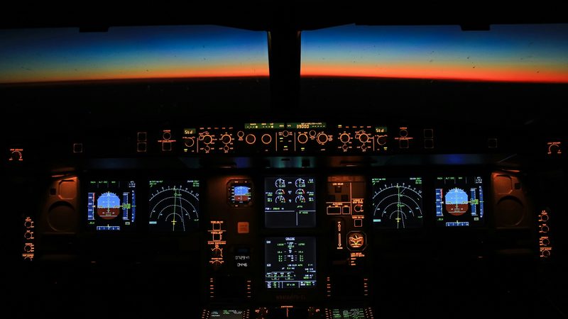 An airliner flight deck at dawn, instruments lit, the aircraft flying itself