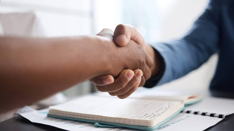 Two people shaking hands over an open notebook and a financial report