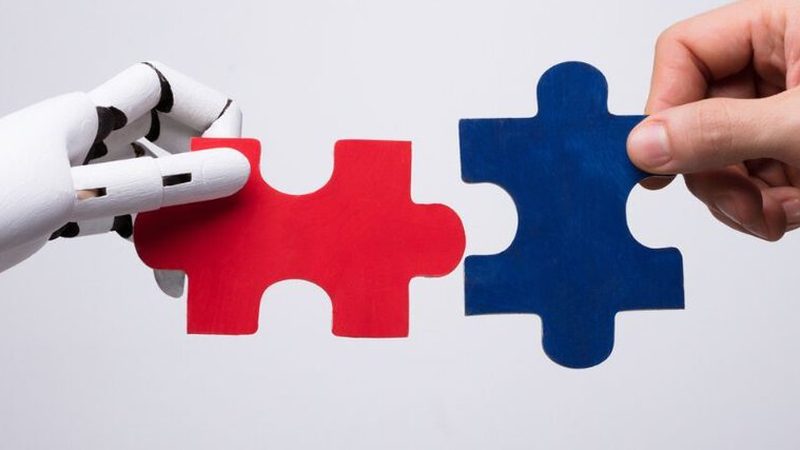 A robotic hand and a human hand fitting two jigsaw pieces together