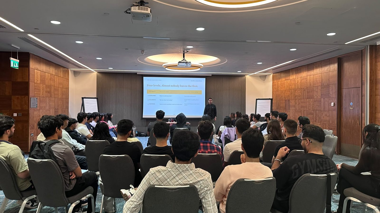 Rahim Hirji presenting the four levels of AI use, from Extract to Extend, to an audience of students and early-career professionals
