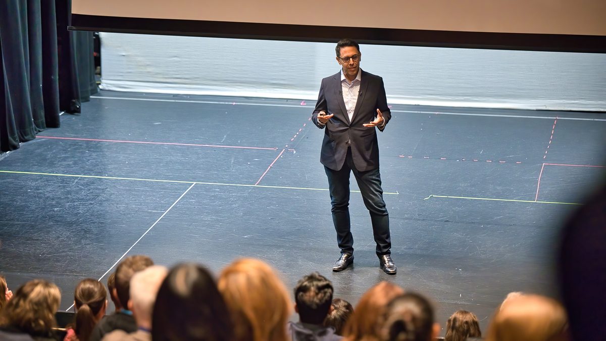 Rahim Hirji giving an evening keynote on stage in London, with the audience in the foreground