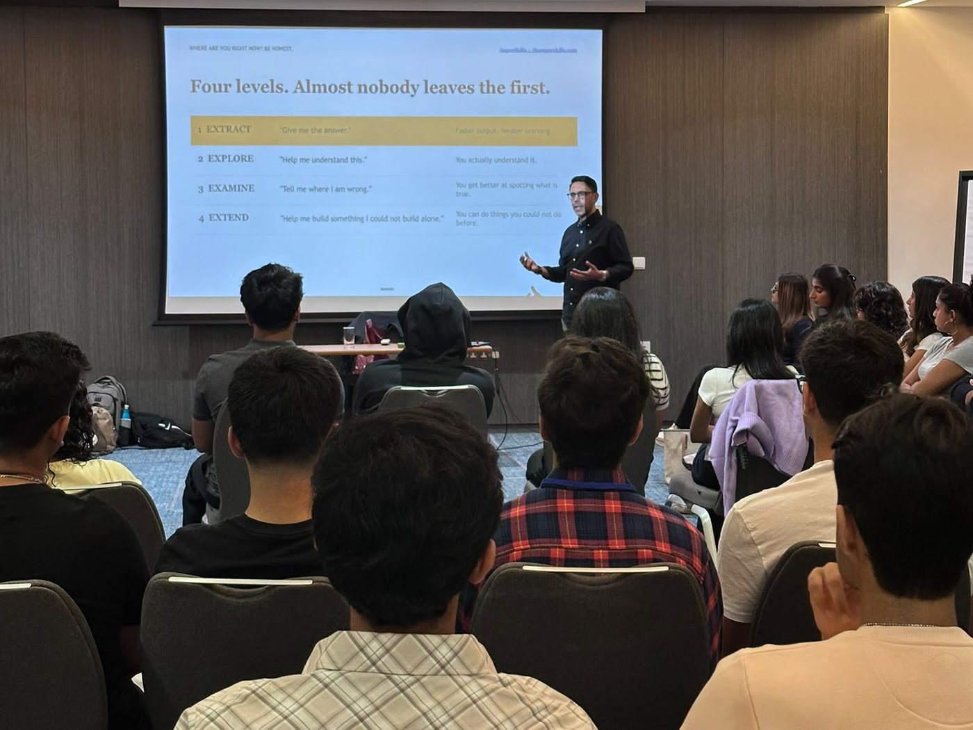 Rahim Hirji presenting the four levels of AI use, Extract, Explore, Examine and Extend, to a room of university students in London