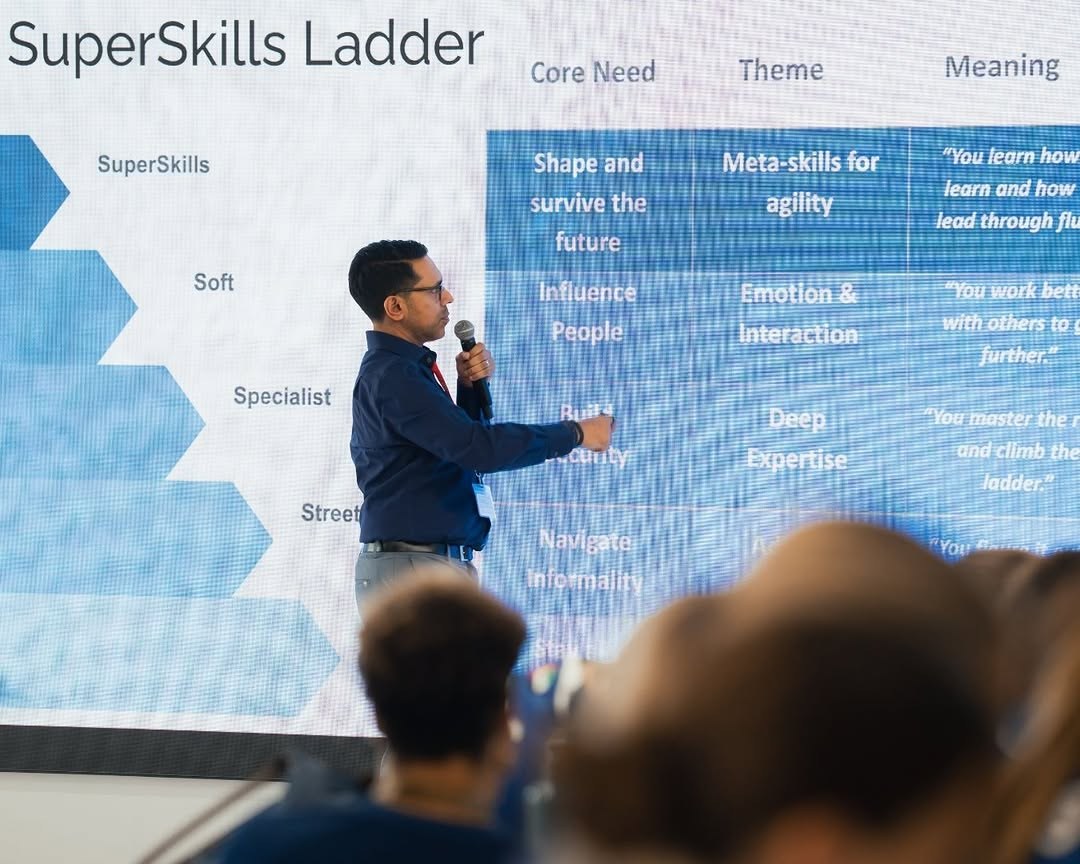 Rahim Hirji speaking with a microphone in front of a projected slide showing the SuperSkills Ladder