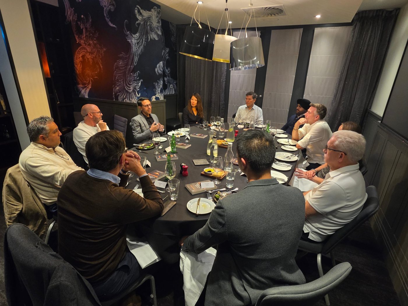 Rahim Hirji talking with a table of senior leaders at a private dinner, copies of SuperSkills on the table
