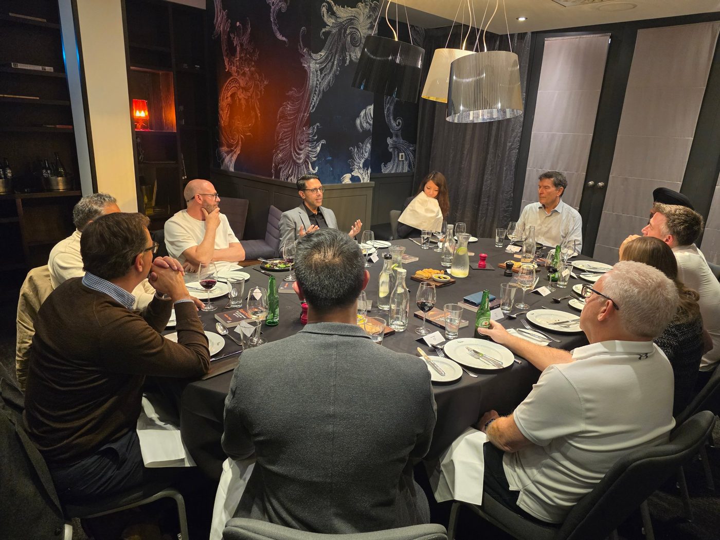 Rahim Hirji speaking at a round dinner table of senior leaders, copies of SuperSkills at each place