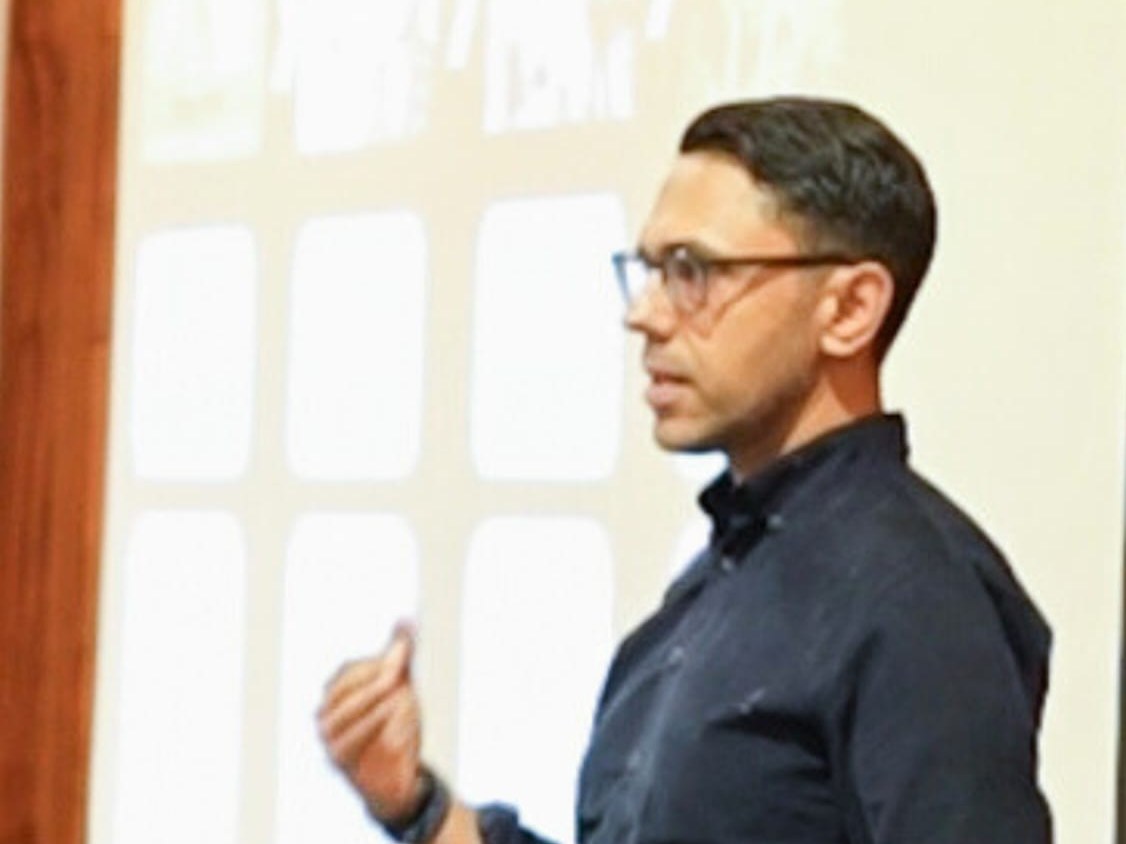 Rahim Hirji speaking without notes beside a projection screen in a seminar room