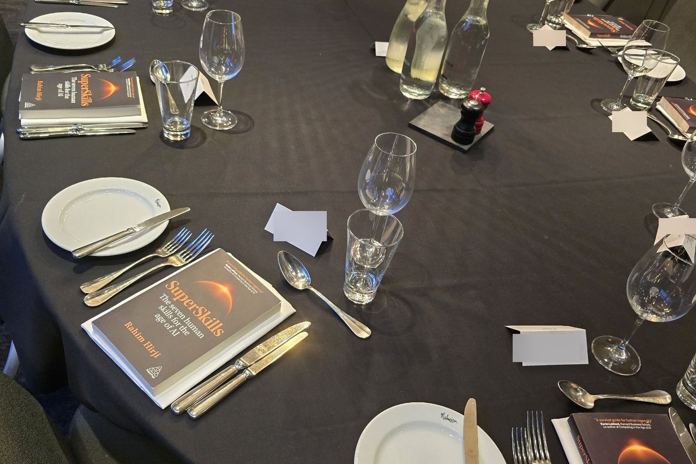 A dinner table laid for a leaders' dinner in London, with a copy of SuperSkills by Rahim Hirji at each place setting