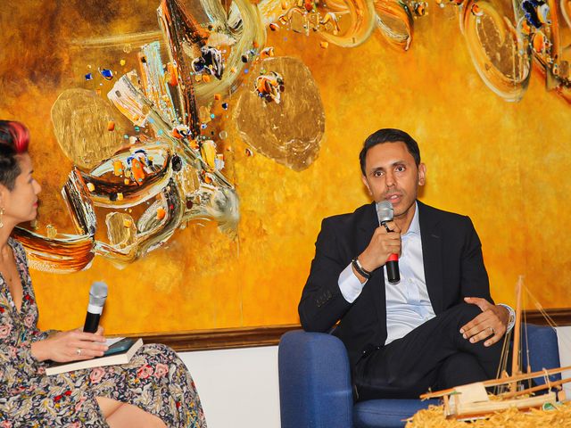 Rahim Hirji in an armchair conversation on stage, microphone in hand